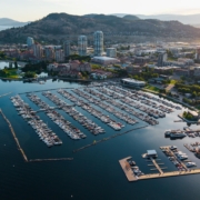 Aerial view of downtown Kelowna, BC, showing Okanagan Lake, City Park, the marina, and surrounding hills in summer